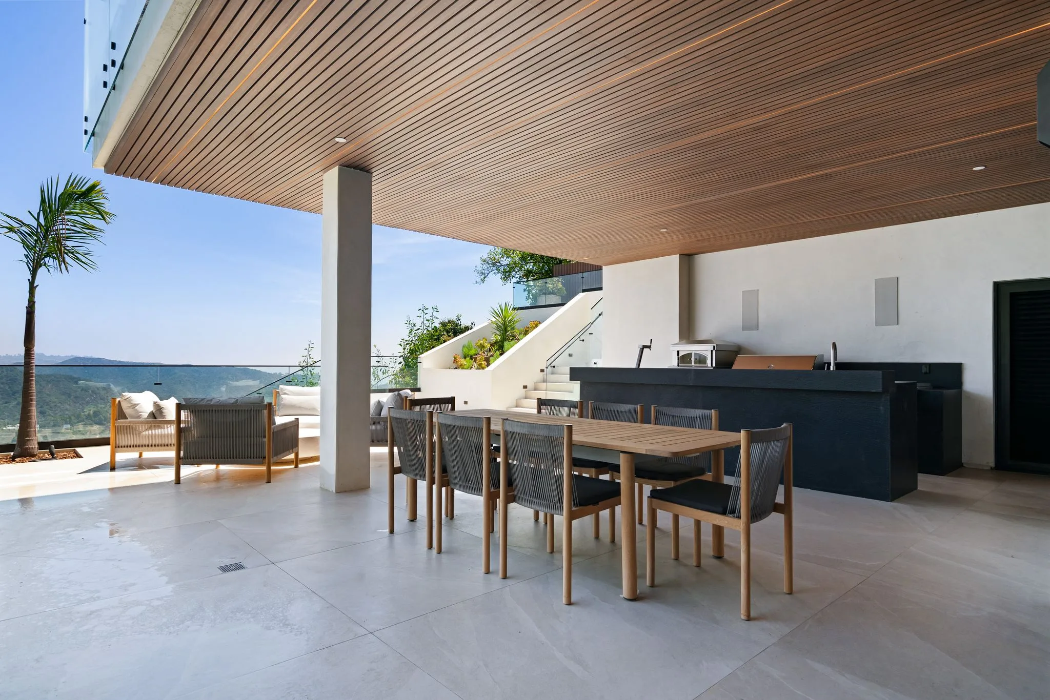 Covered terrace with long dining table, built-in grill counter and steps climbing past planted beds