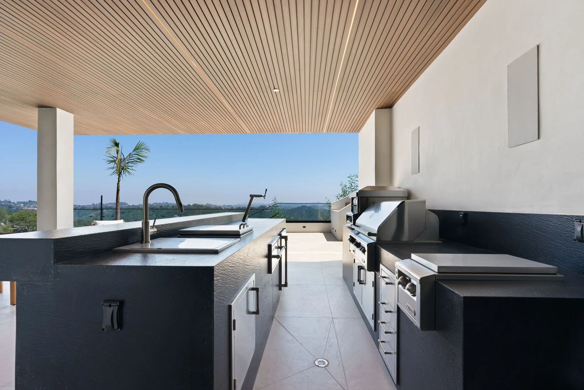Outdoor kitchen with stainless grill, griddle and sink set into black counters, canyon view straight ahead
