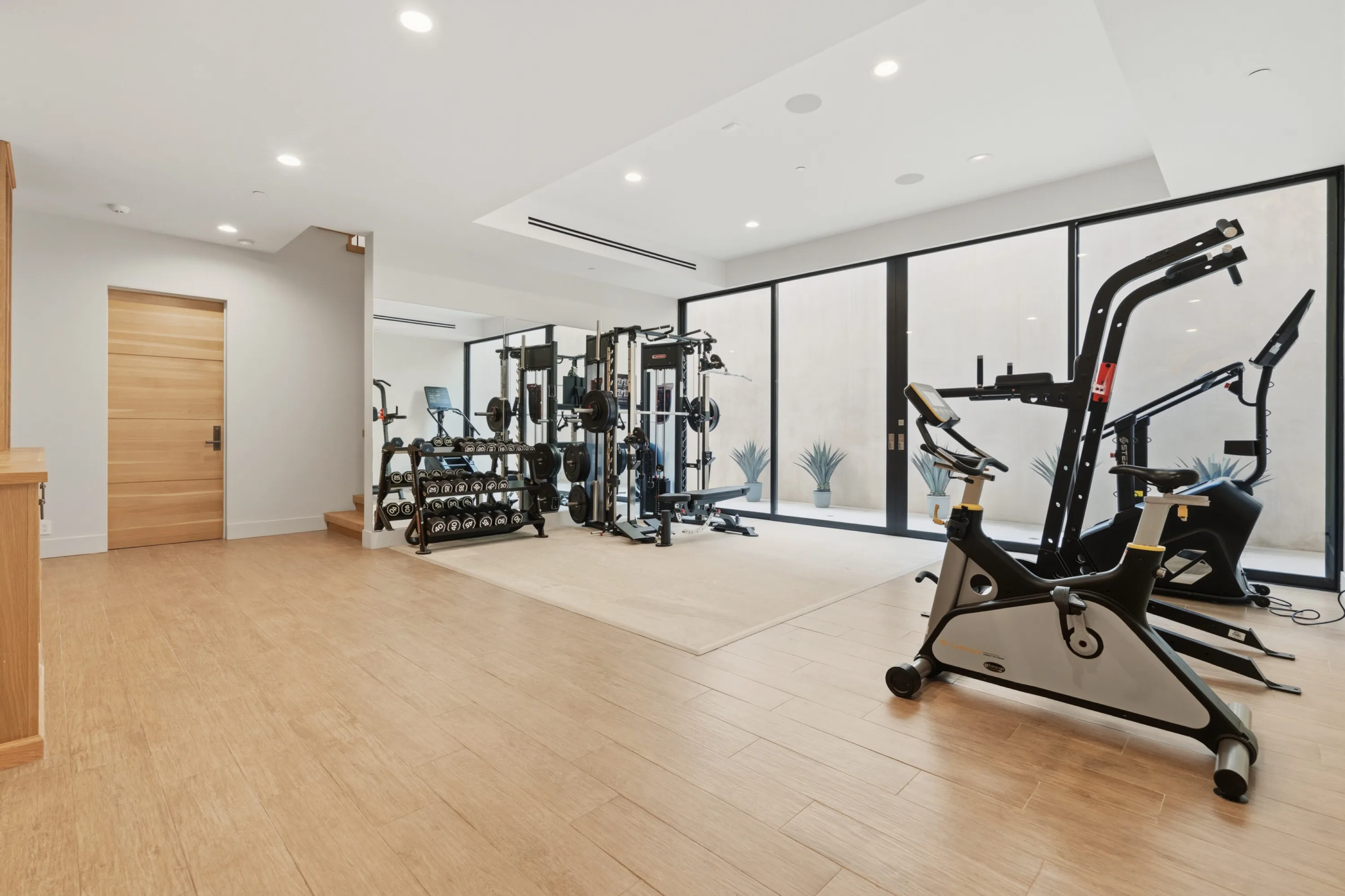 Private gym with free weights, cable machine and exercise bikes beside a wall of glass