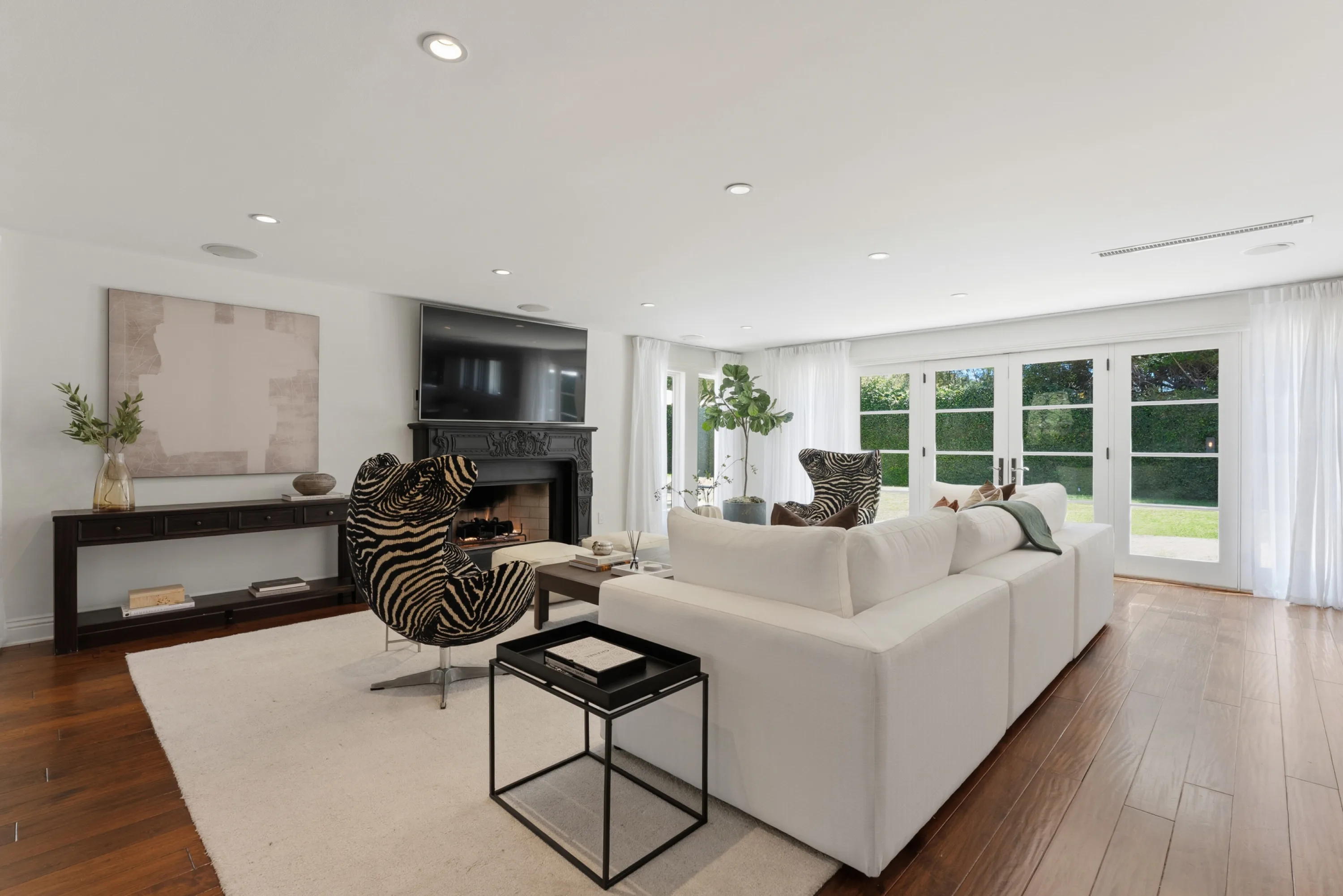 Family lounge with carved black fireplace, wall-mounted TV and French doors onto the lawn