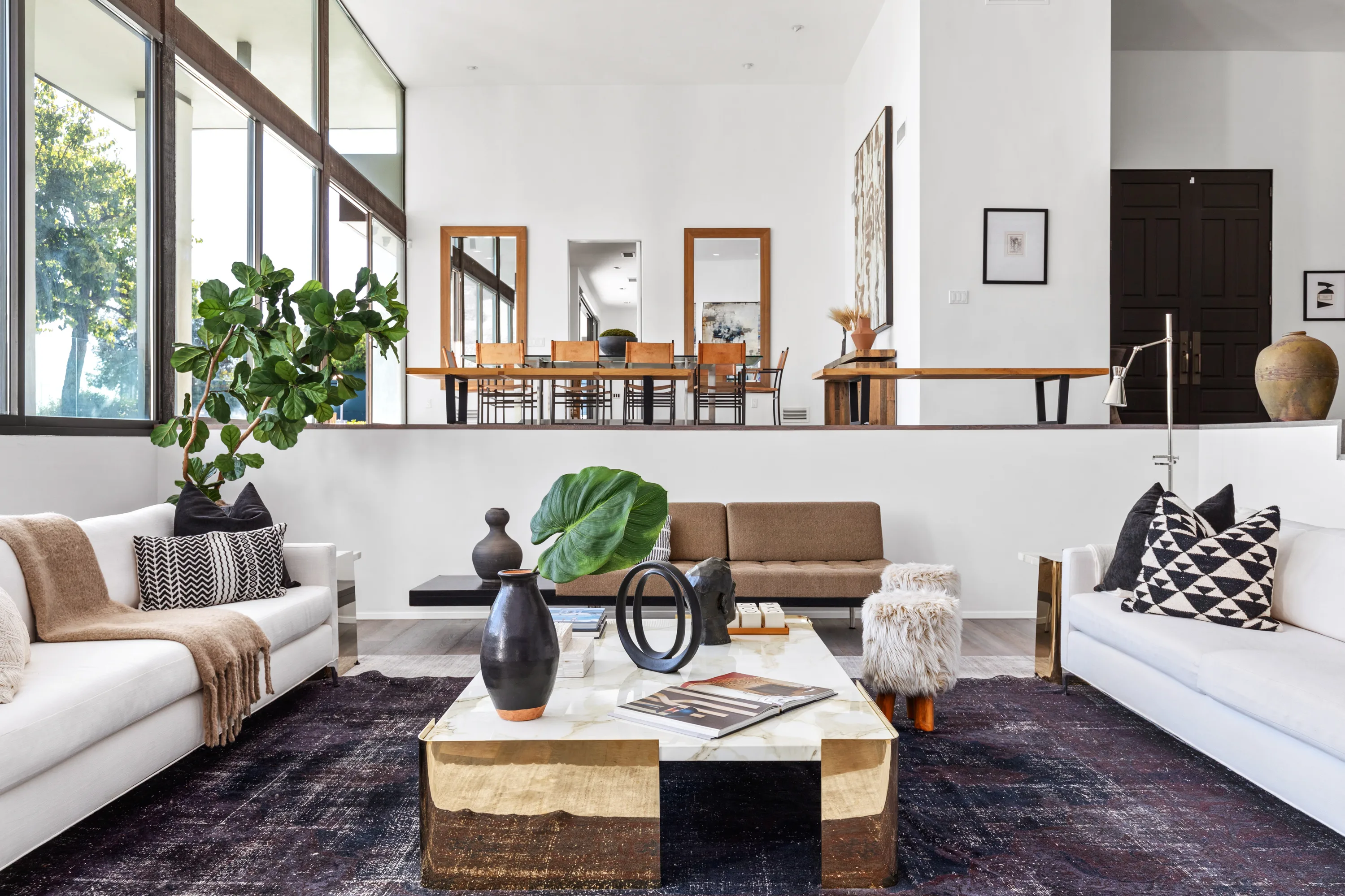 Sunken lounge with facing white sofas and brass coffee table below the raised dining room