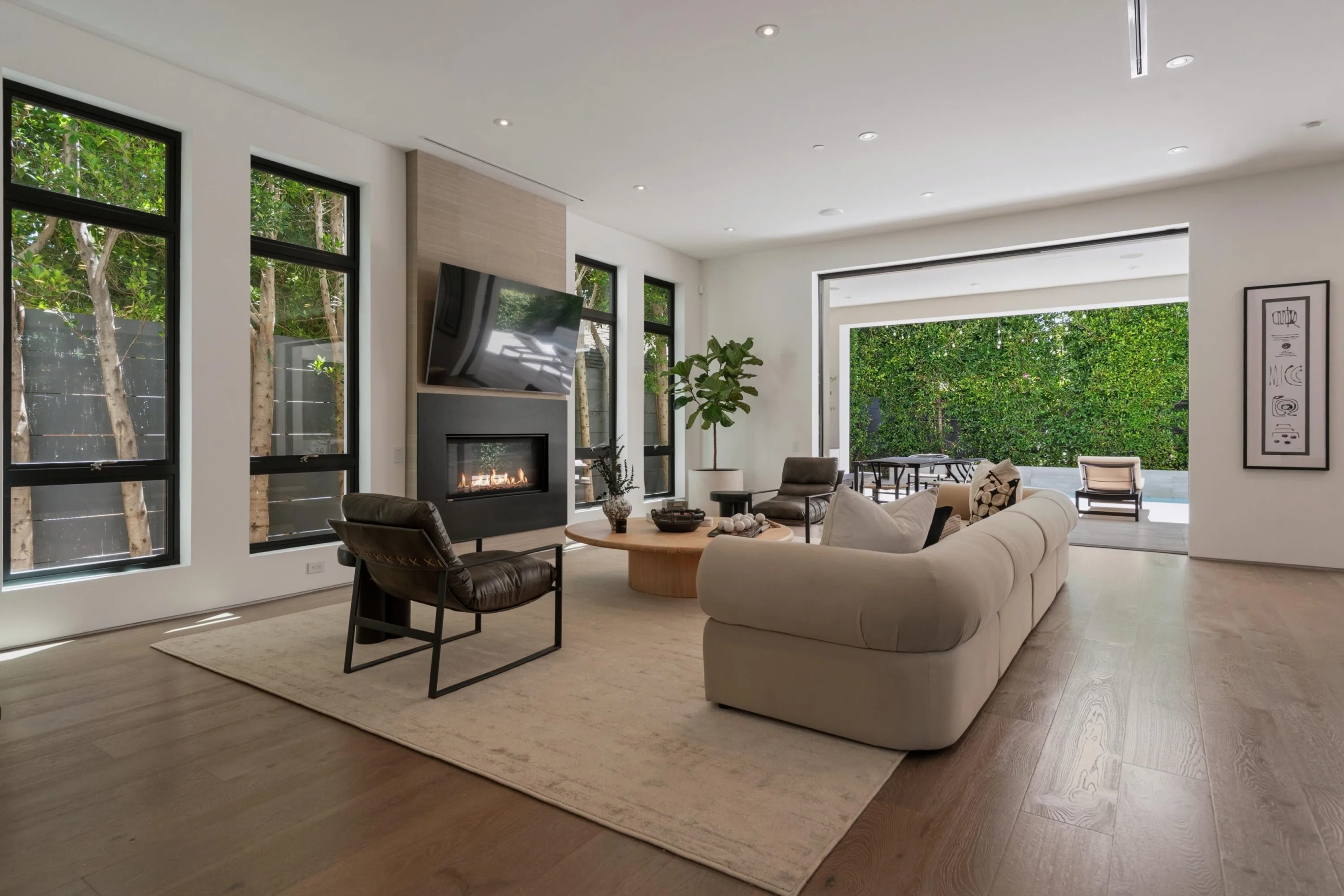 Fireplace lounge opening through a pocketing glass wall to the hedged pool deck