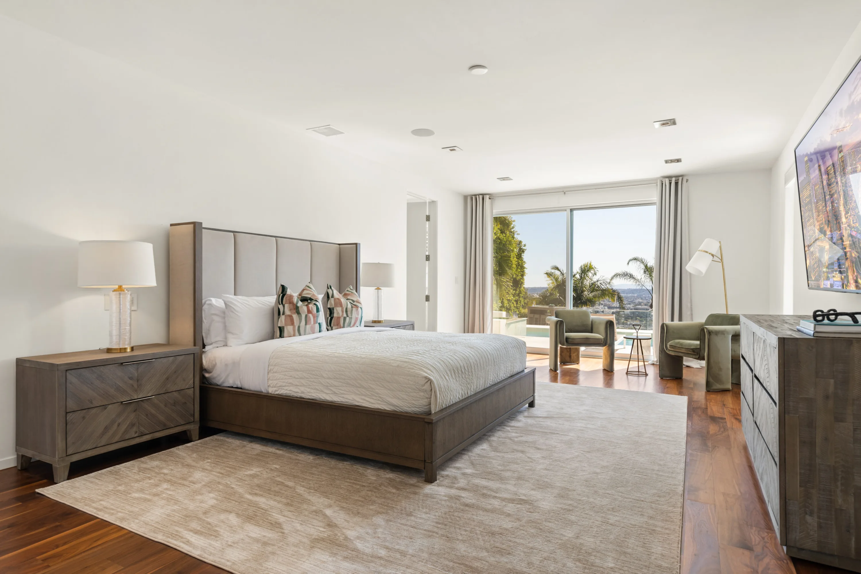 Primary suite with upholstered king bed, lounge chairs and sliding doors onto the pool deck