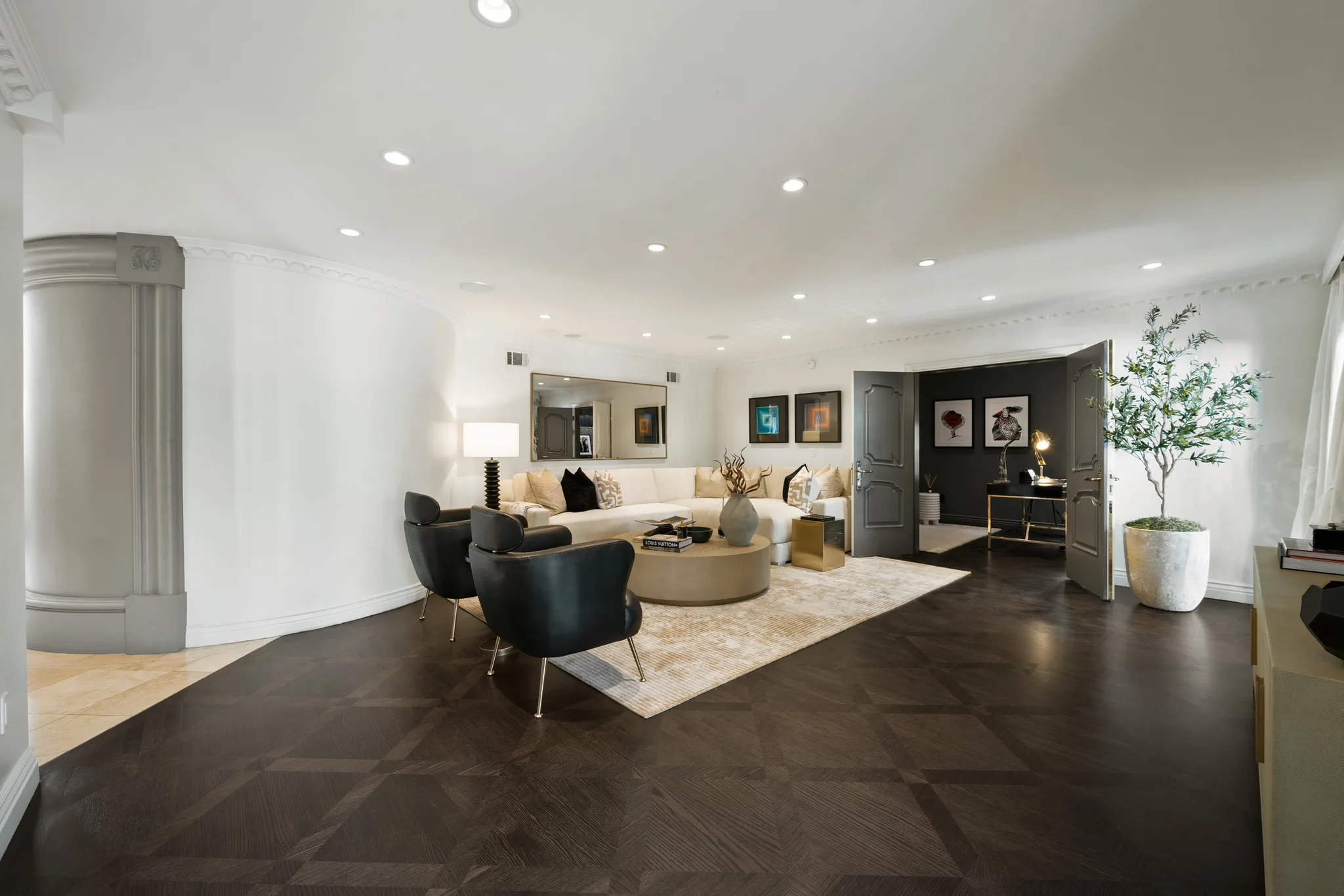 Curved-wall living area looking through open doors to a dark-walled study and potted olive tree
