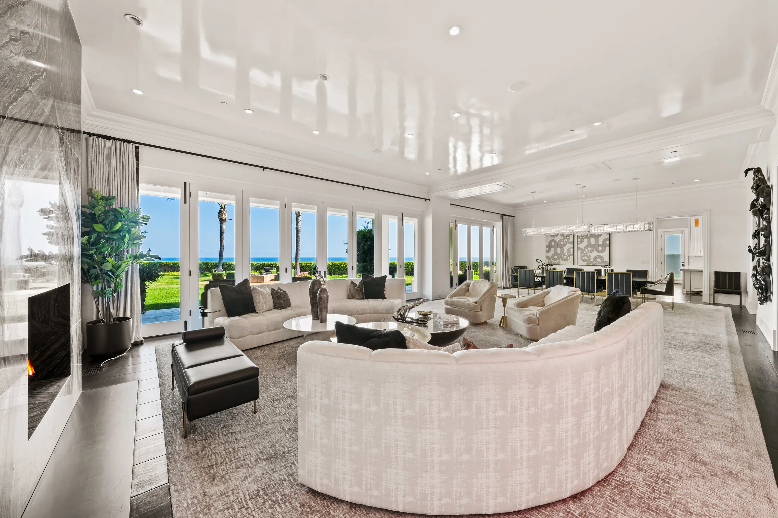 Great room with curved ivory sectionals, stone fireplace and folding glass doors opening to lawn and ocean
