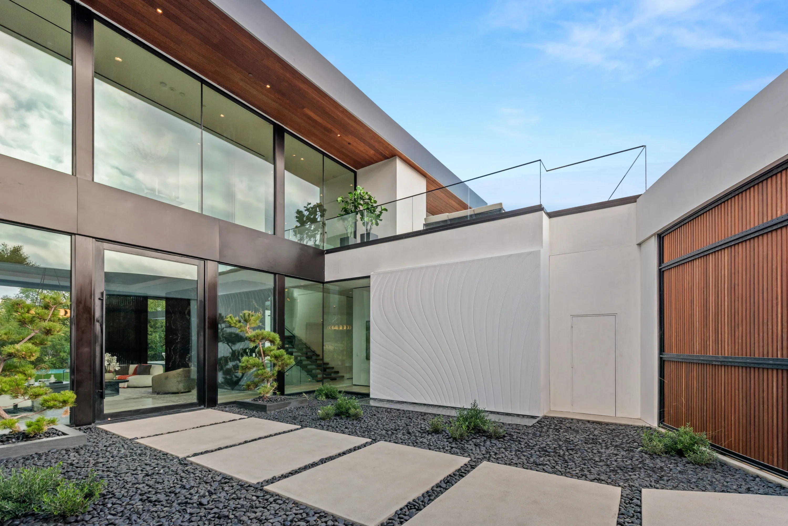 Entry courtyard of black gravel and stepping-stone pavers leading to the glazed front door and stair hall