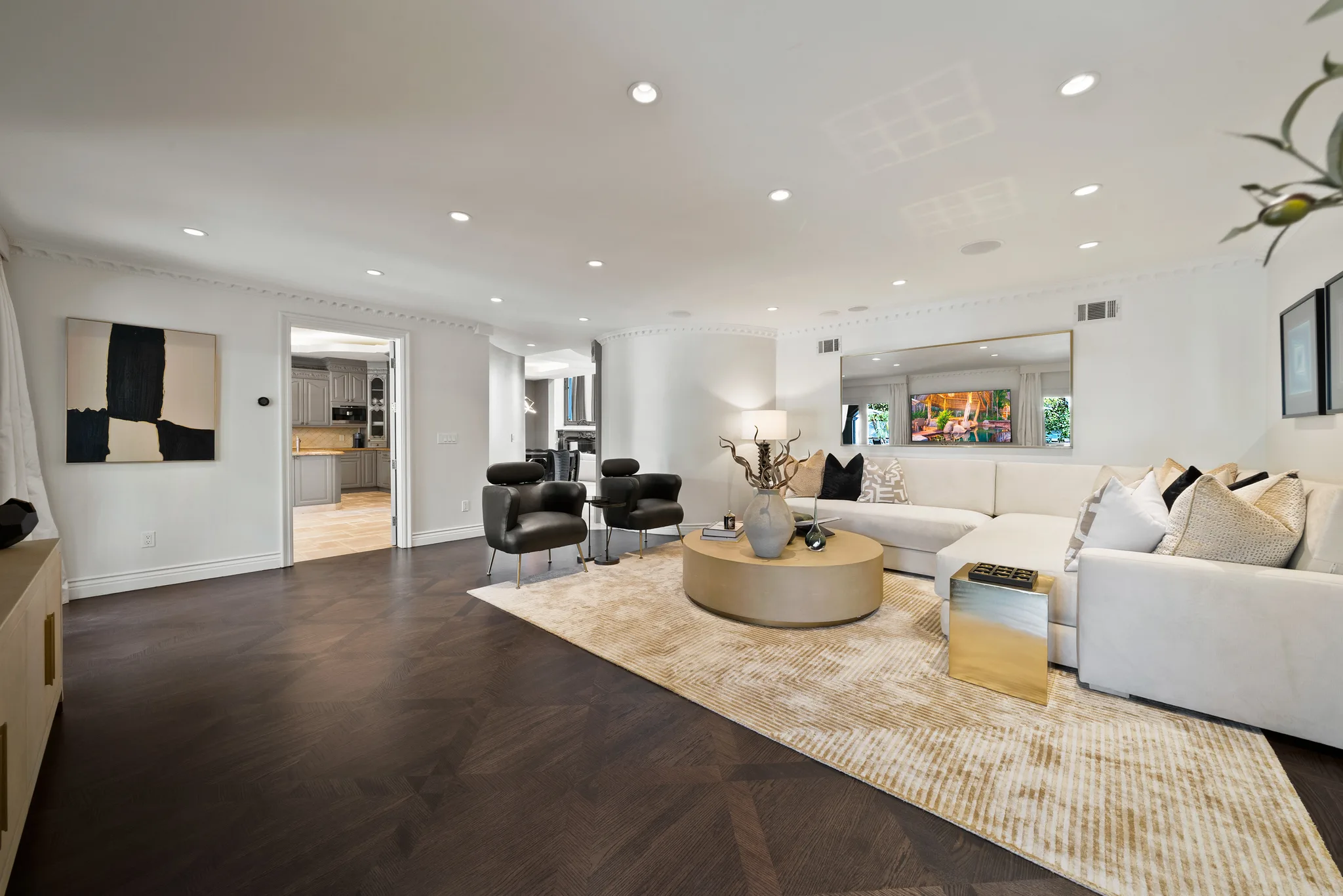 Open lounge on dark parquet floors, sectional and wall-mounted screen beside the kitchen doorway