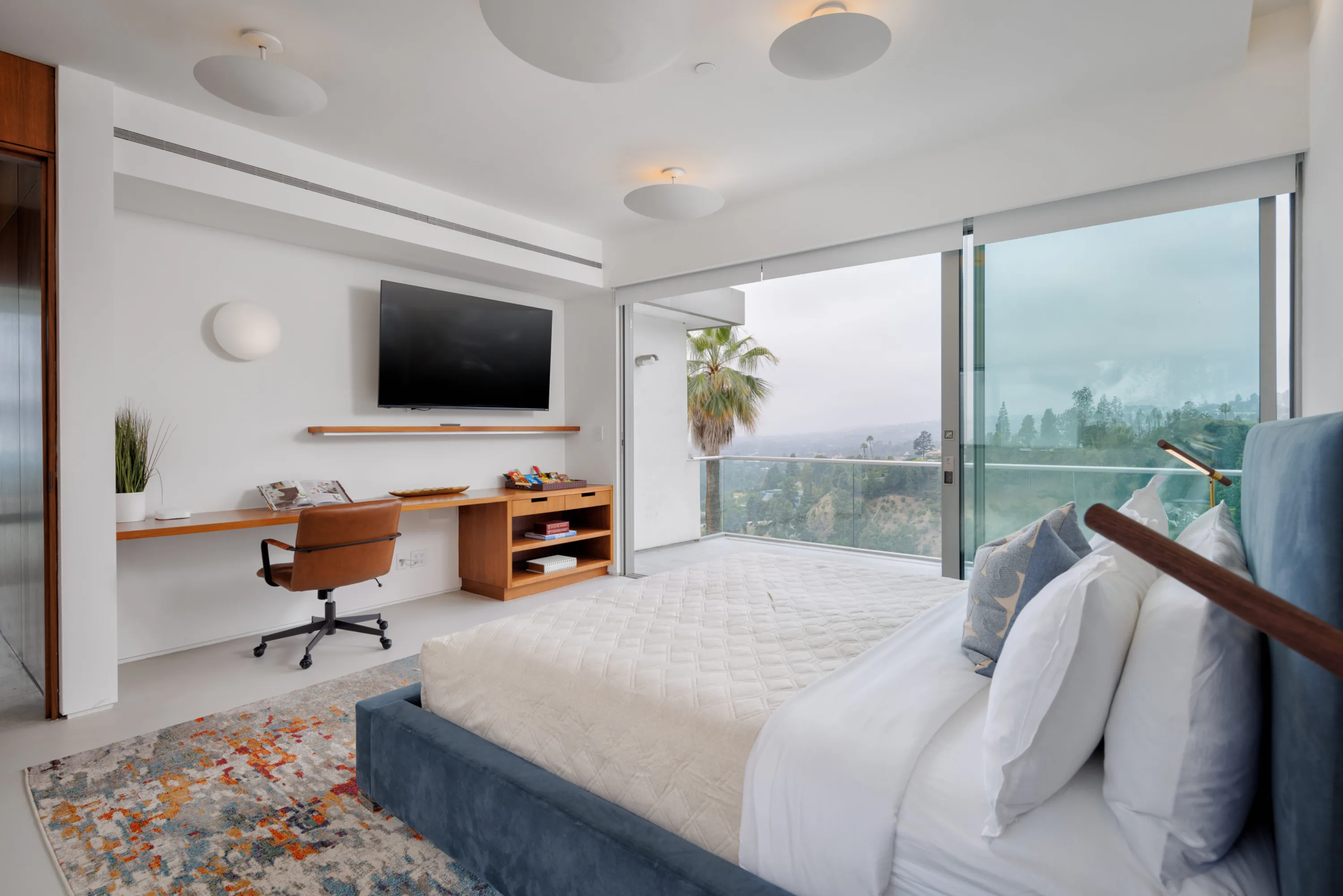 Primary suite with blue velvet bed, built-in desk and sliding glass doors opening to a canyon-view balcony
