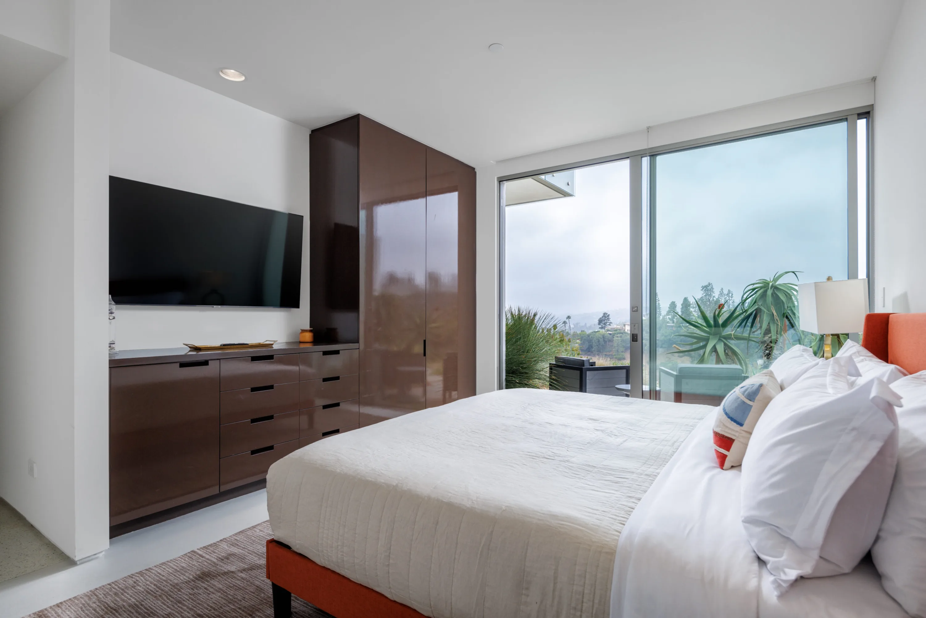 Bedroom in burnt orange and lacquered walnut, sliding glass leading to a planted terrace with seating