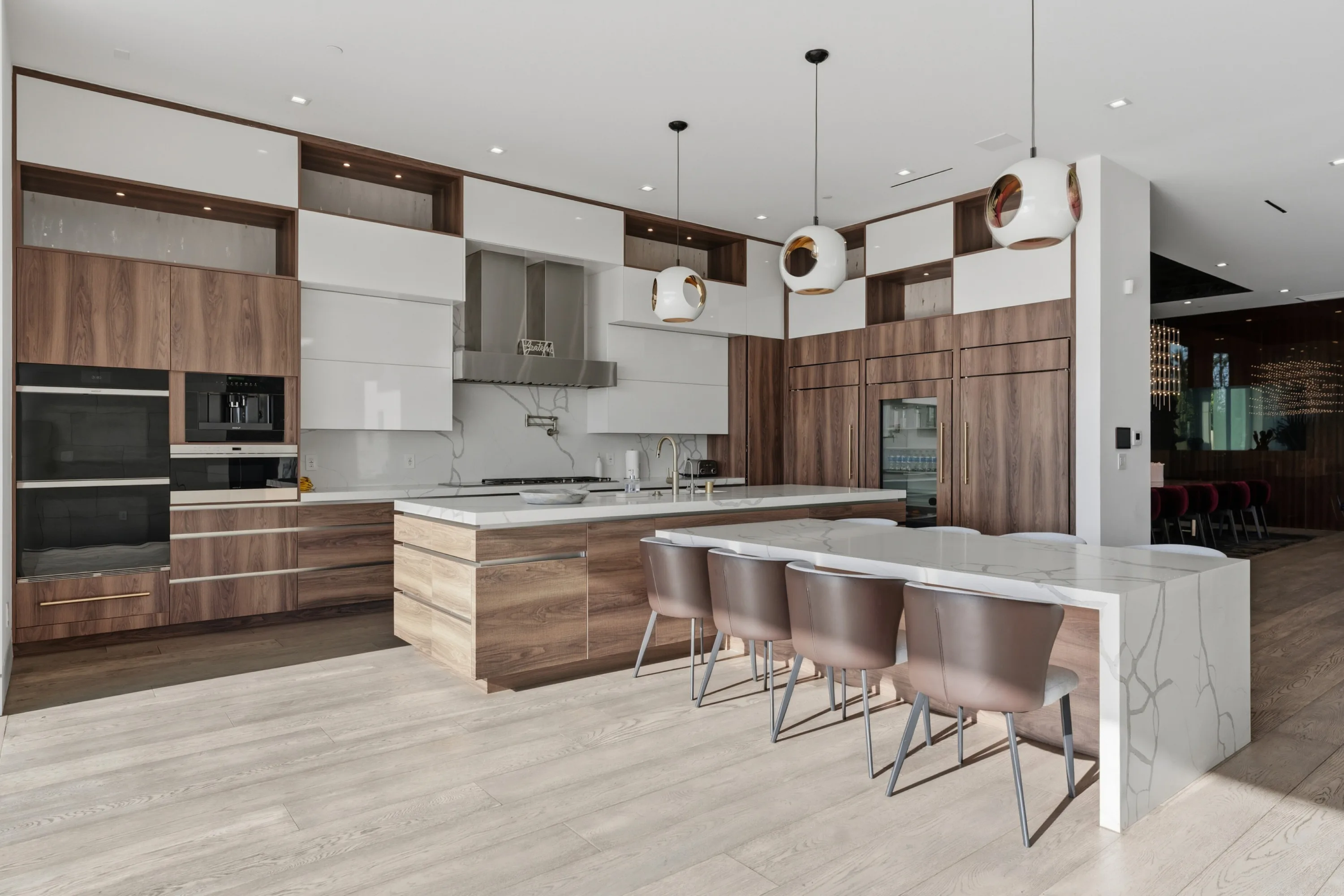 Chef's kitchen with double ovens, walnut cabinetry and a marble breakfast bar seating four under copper pendants