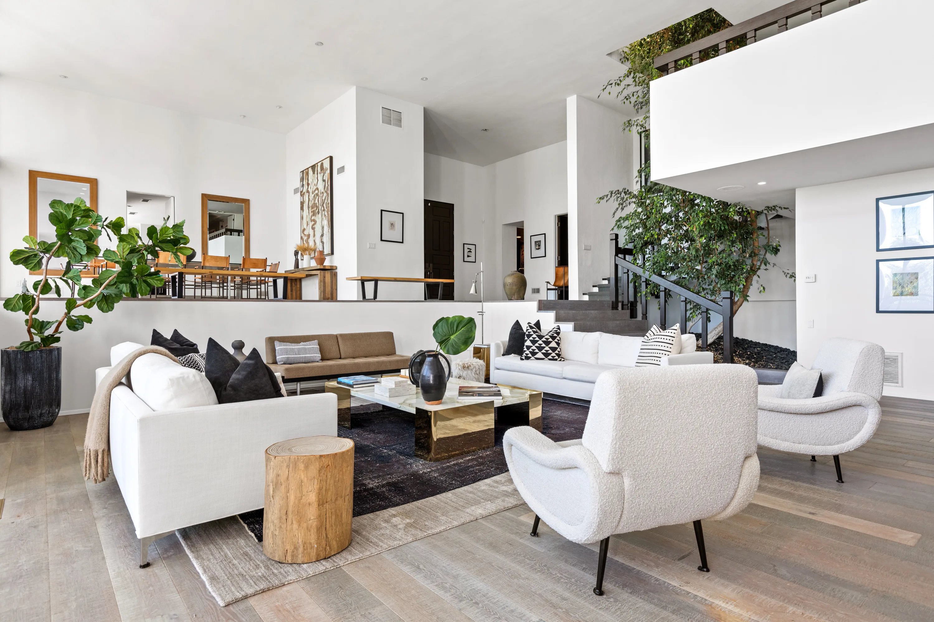 Open-plan great room with boucle armchairs, indoor tree and staircase rising to the mezzanine
