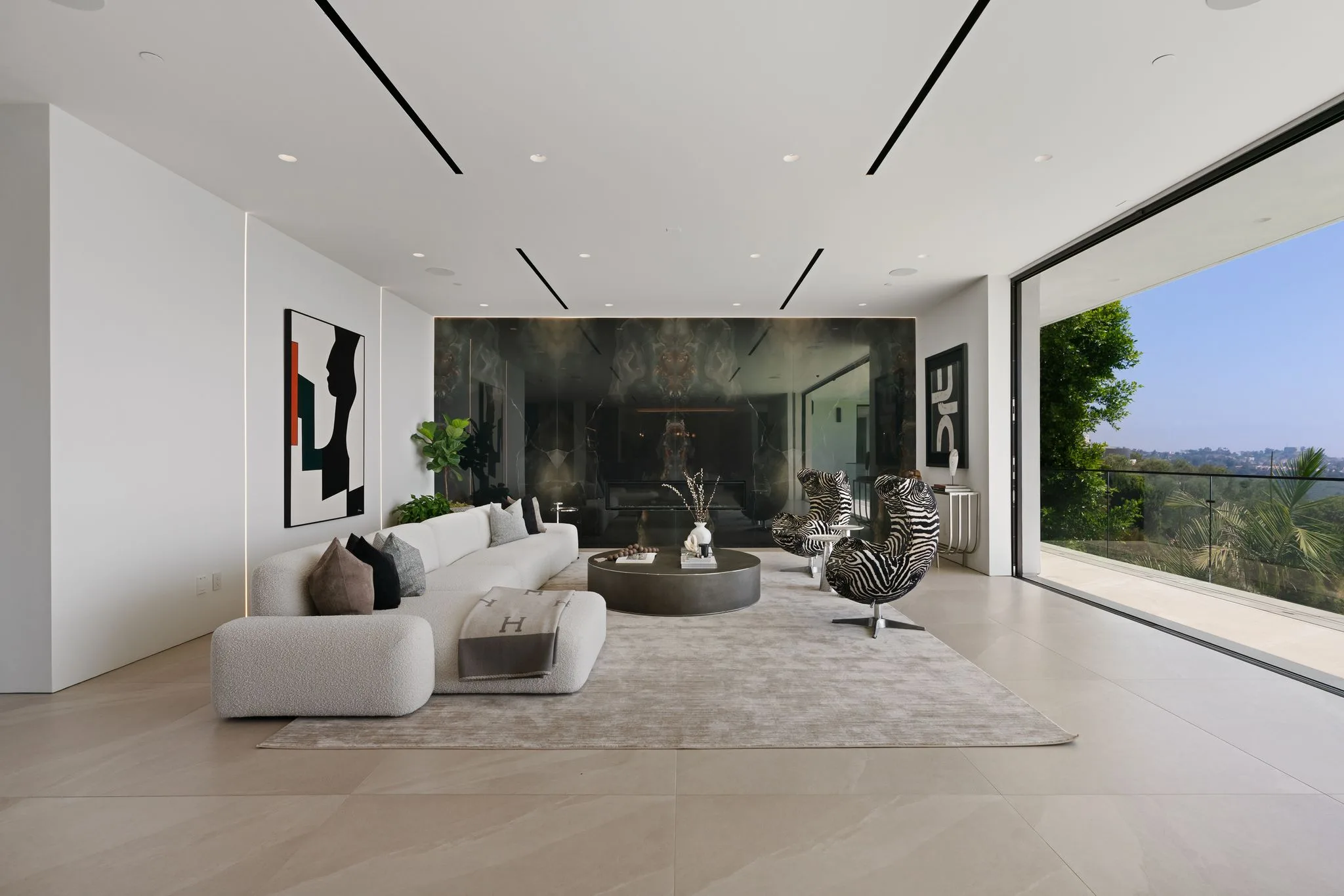 Main living room with bouclé sectional, zebra-print swivel chairs and a dark stone fireplace wall