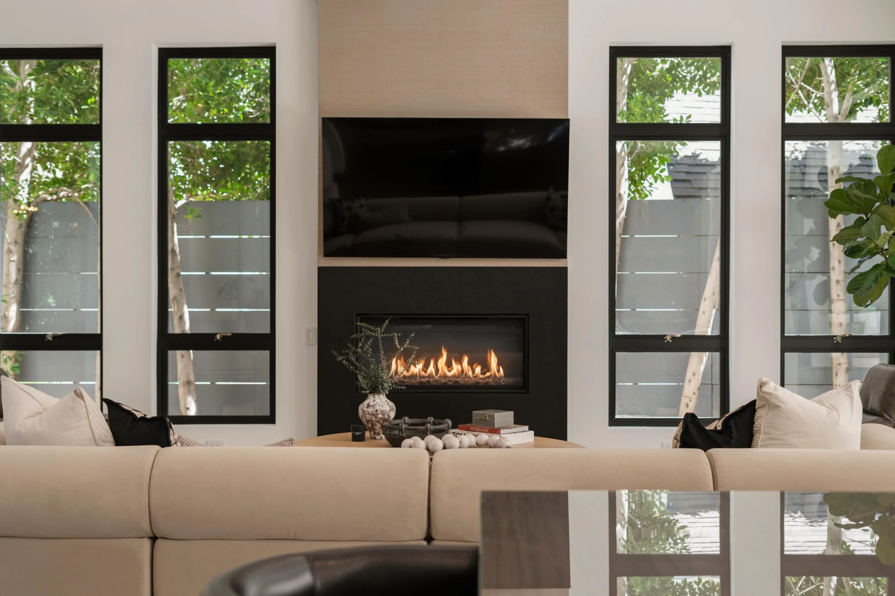 Lit linear gas fireplace and wall-mounted TV framed by narrow floor-to-ceiling windows above the living room sofa