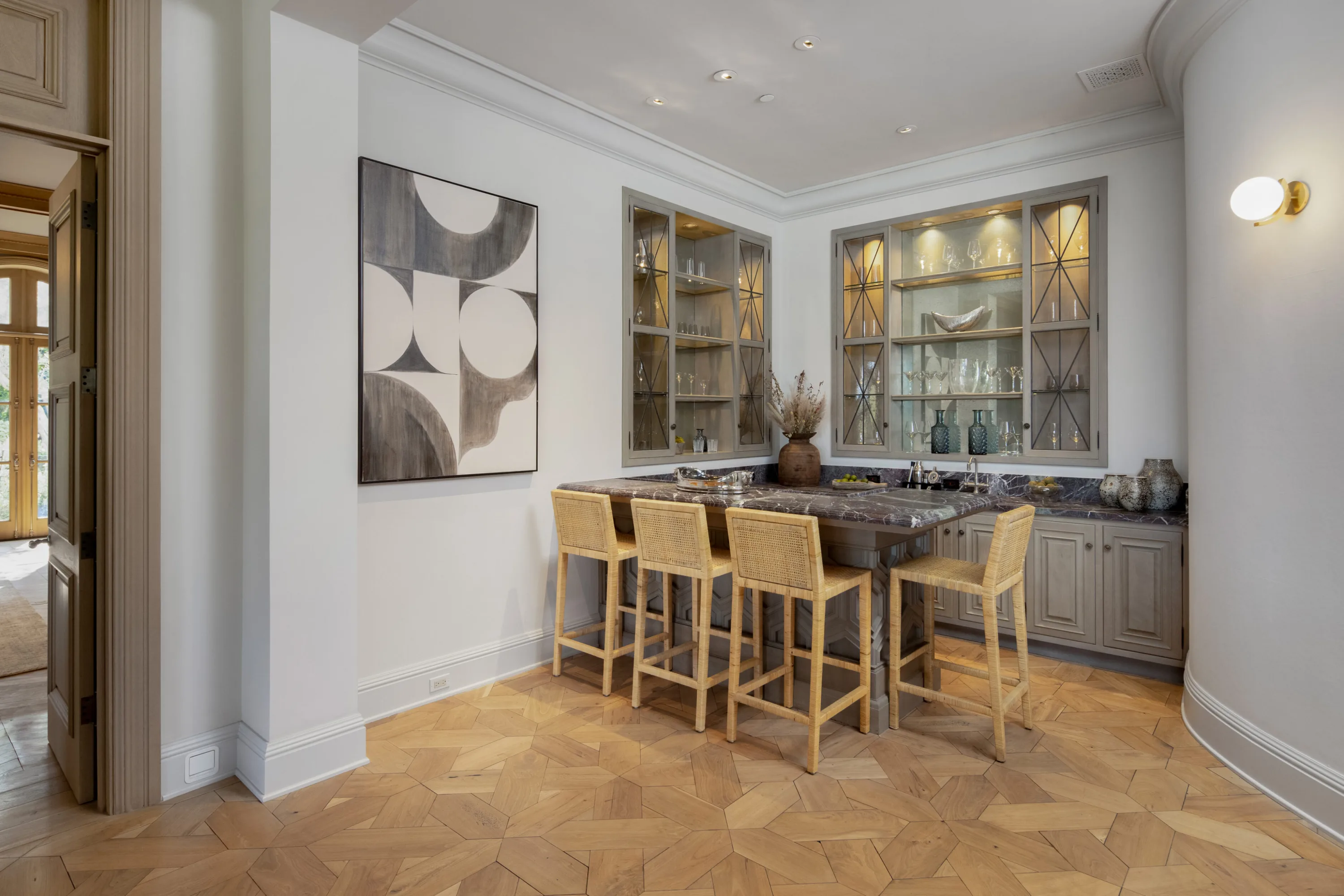 Butler's bar with dark marble counter, cane counter stools and lit glass-front cabinets of stemware