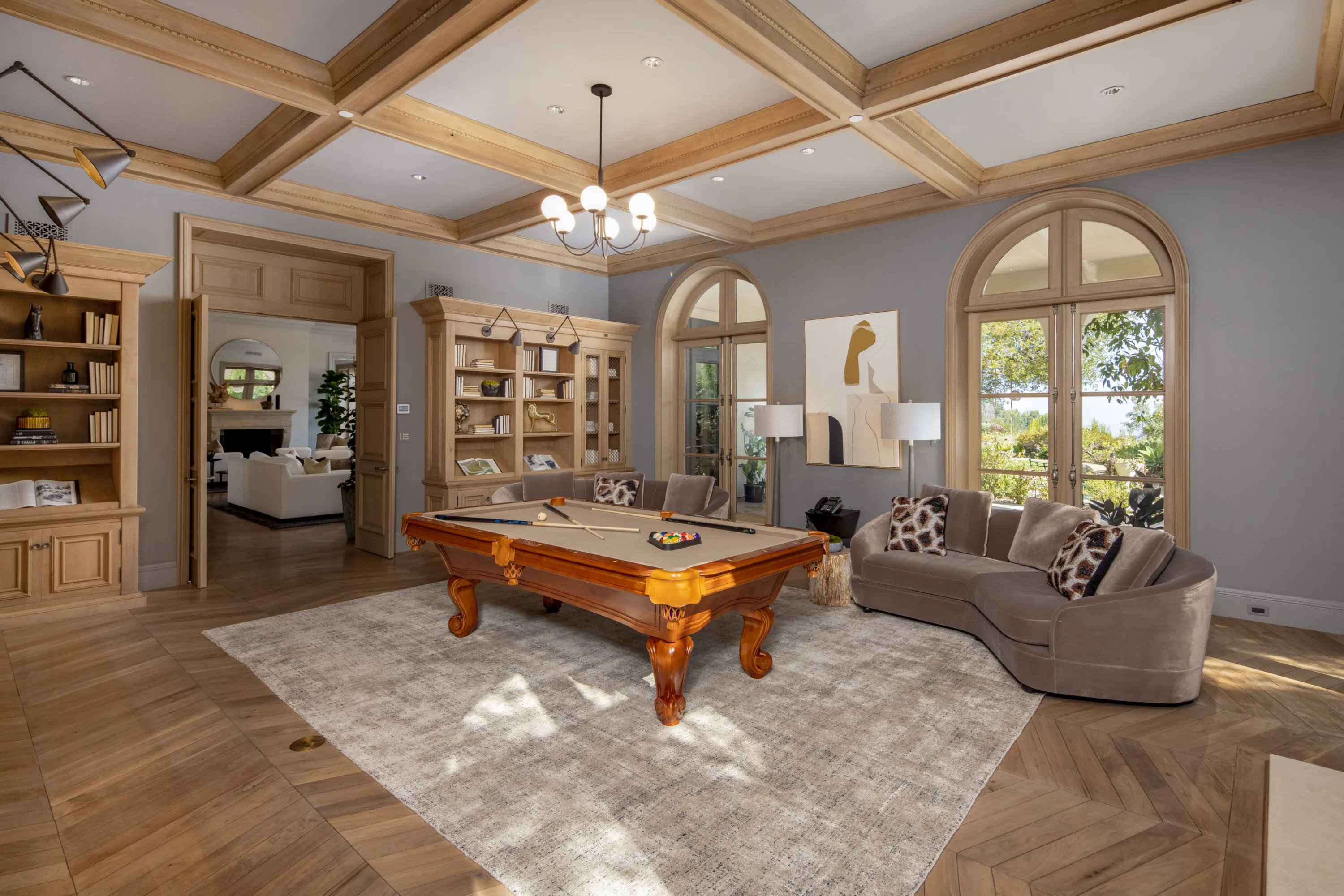 Billiards room under a coffered beam ceiling, pool table, curved velvet sofa and arched doors to the garden