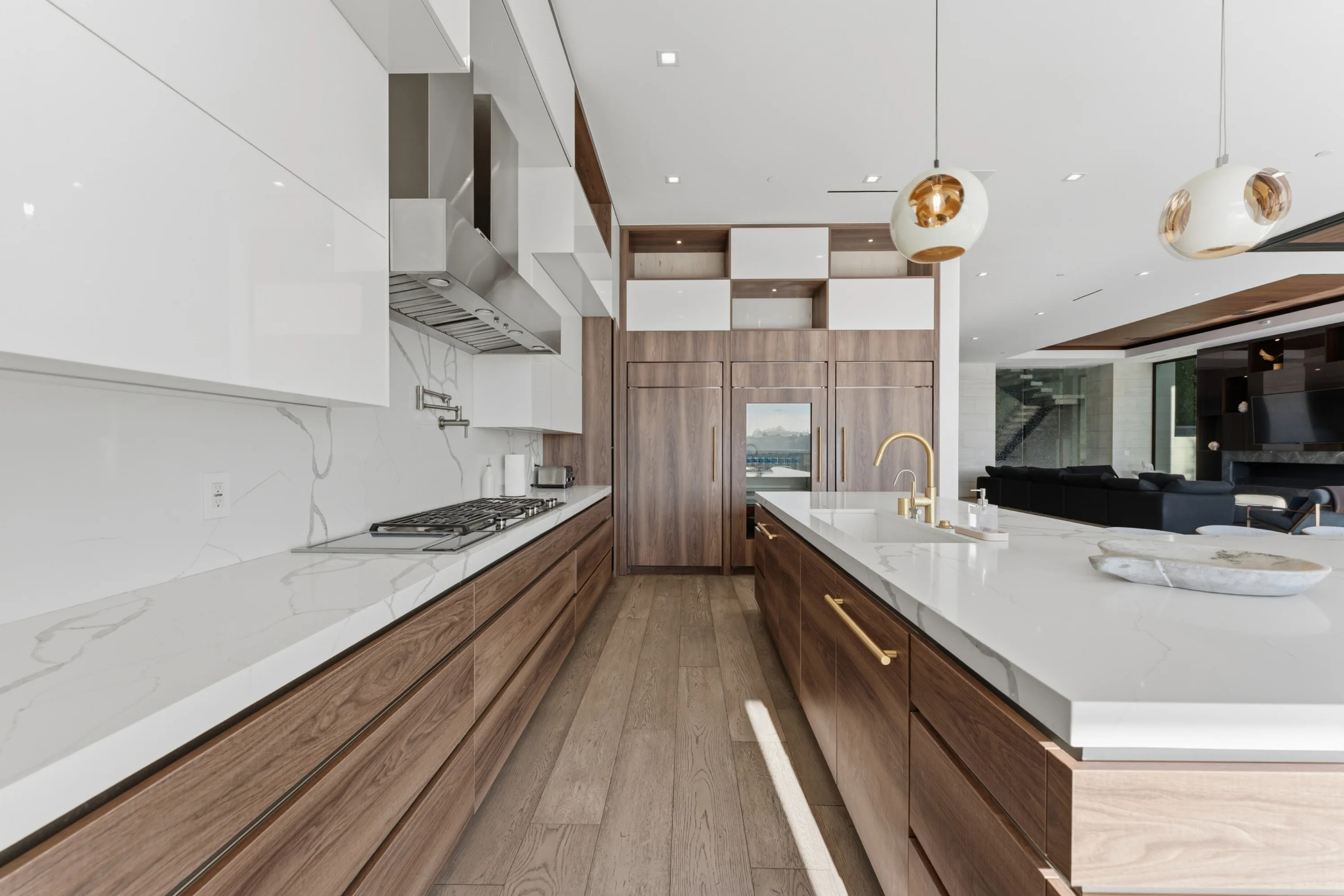Galley view of the kitchen: gas range, veined stone counters and brass tap, with the family room framed beyond