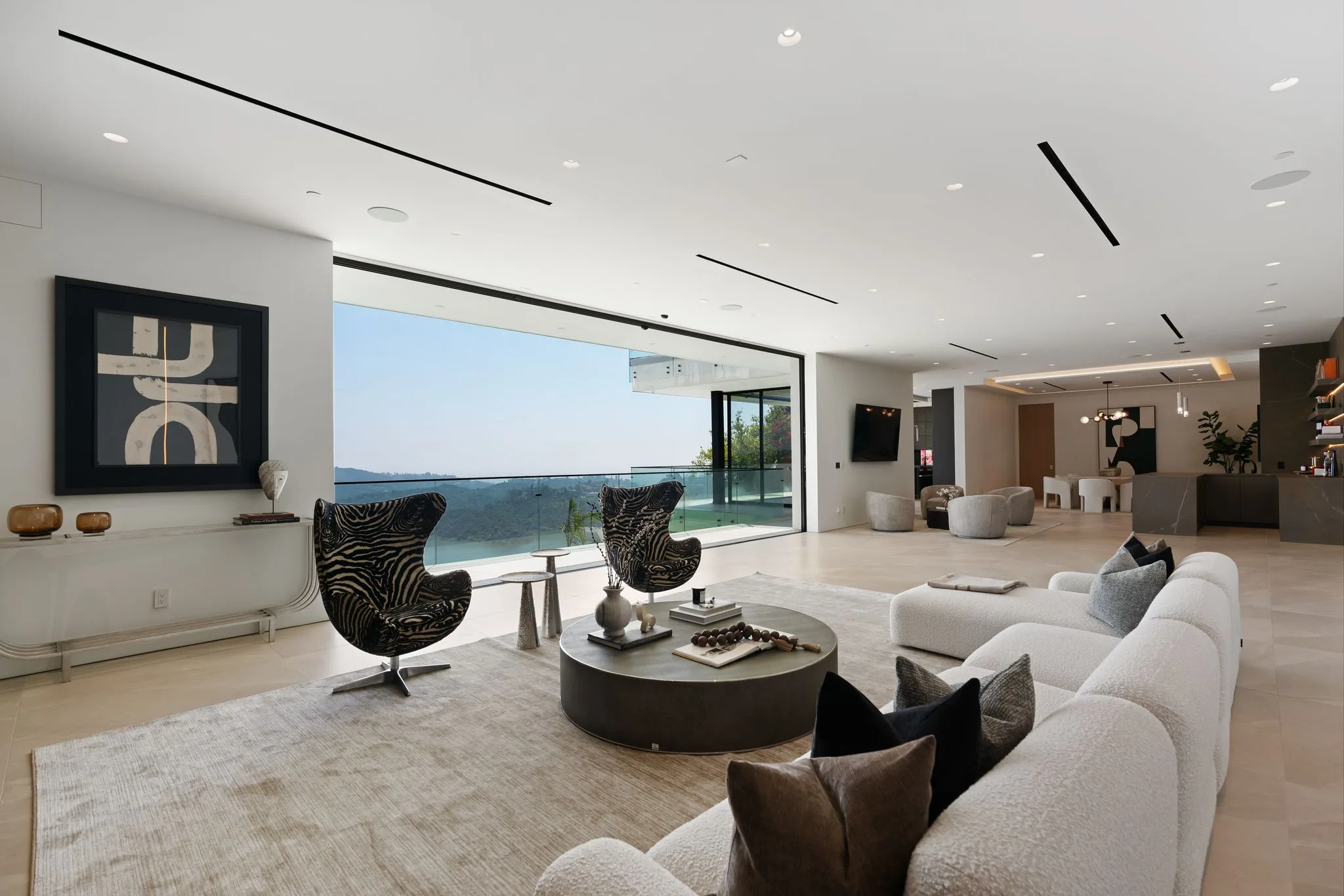 Living room opening through a full-width glass wall to the canyon, kitchen and dining beyond