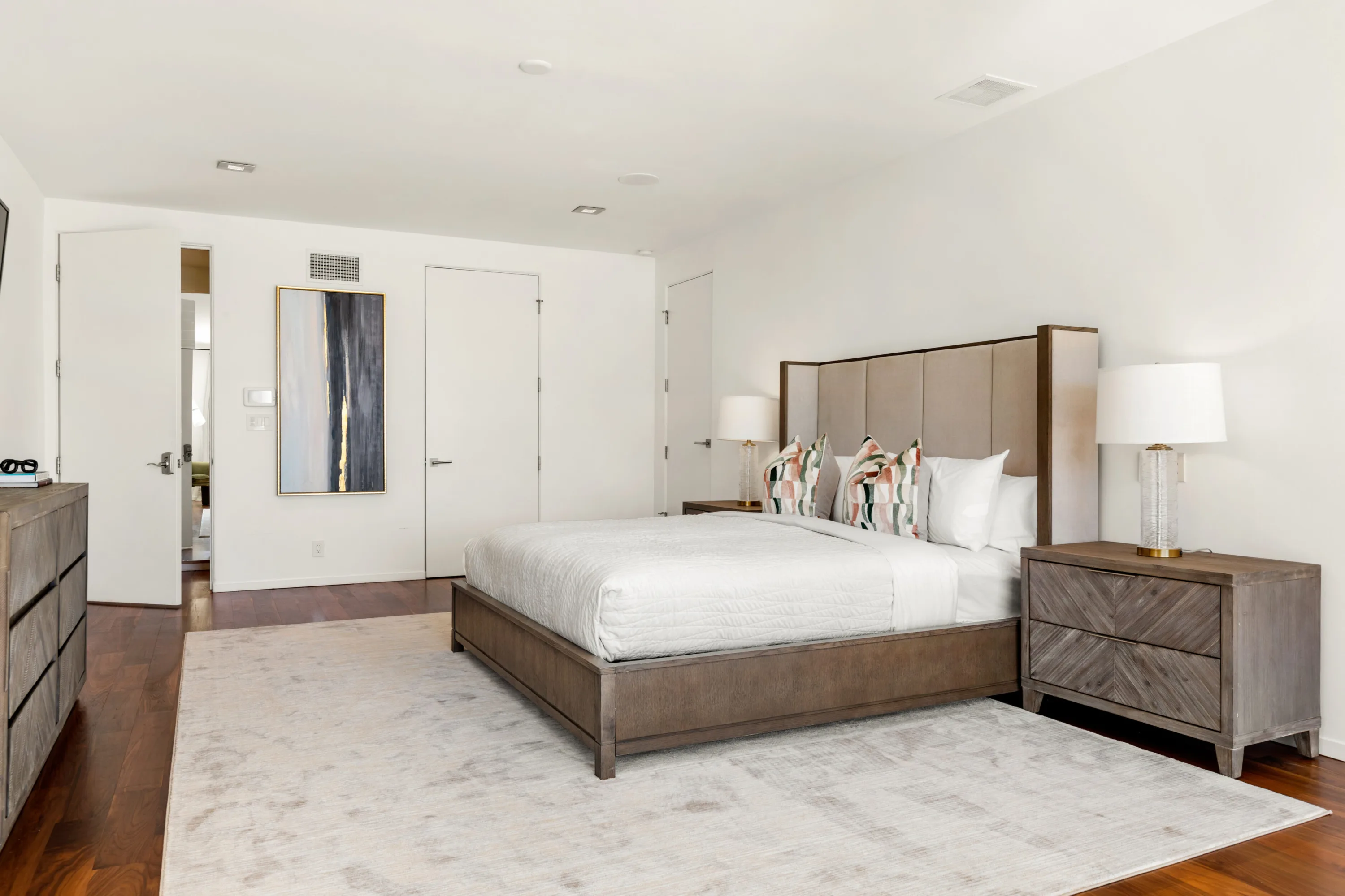 Guest bedroom with wingback headboard, matching nightstands and abstract canvas beside the closet doors