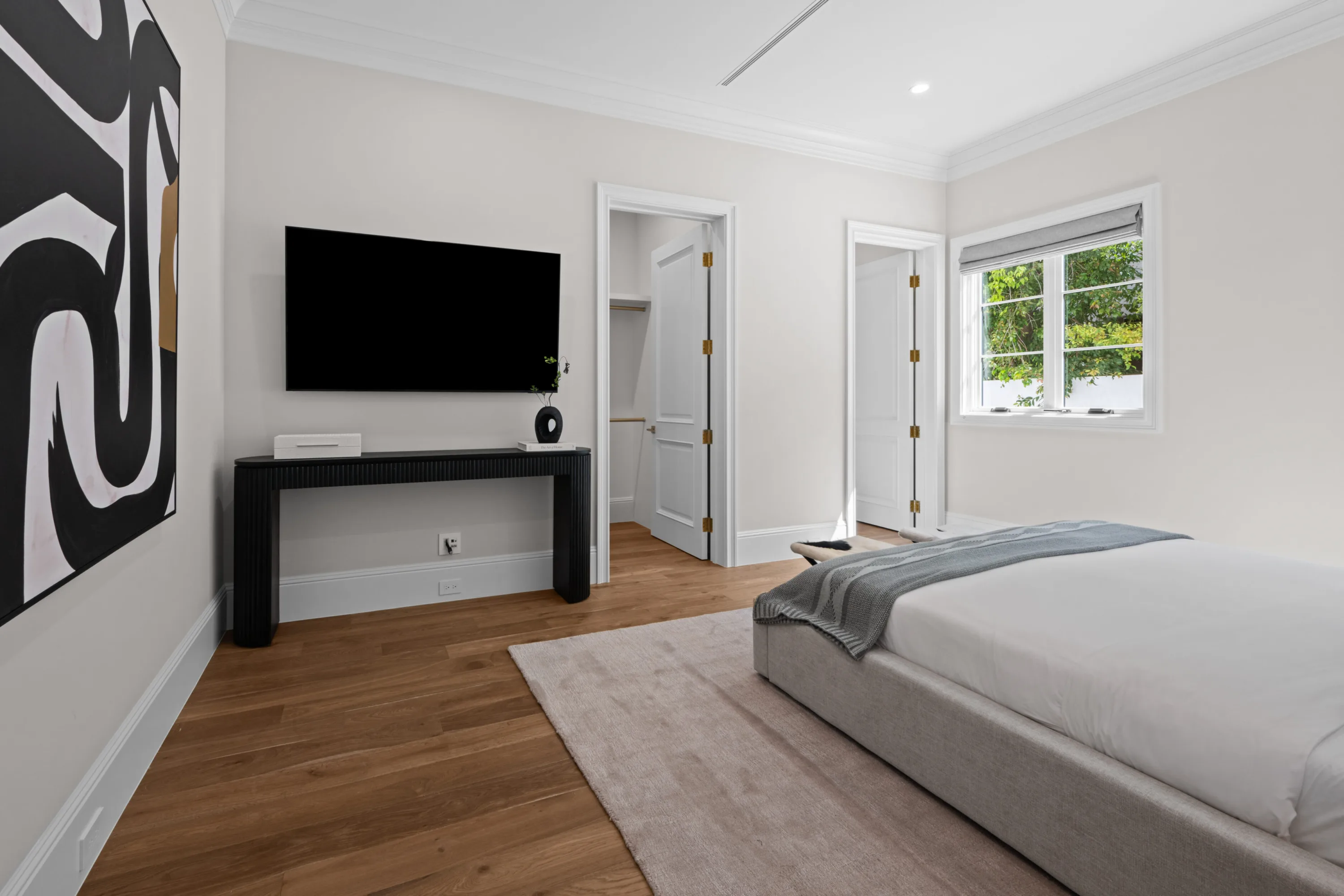Guest bedroom with wall-mounted TV, fluted console, walk-in closet and a garden-facing window