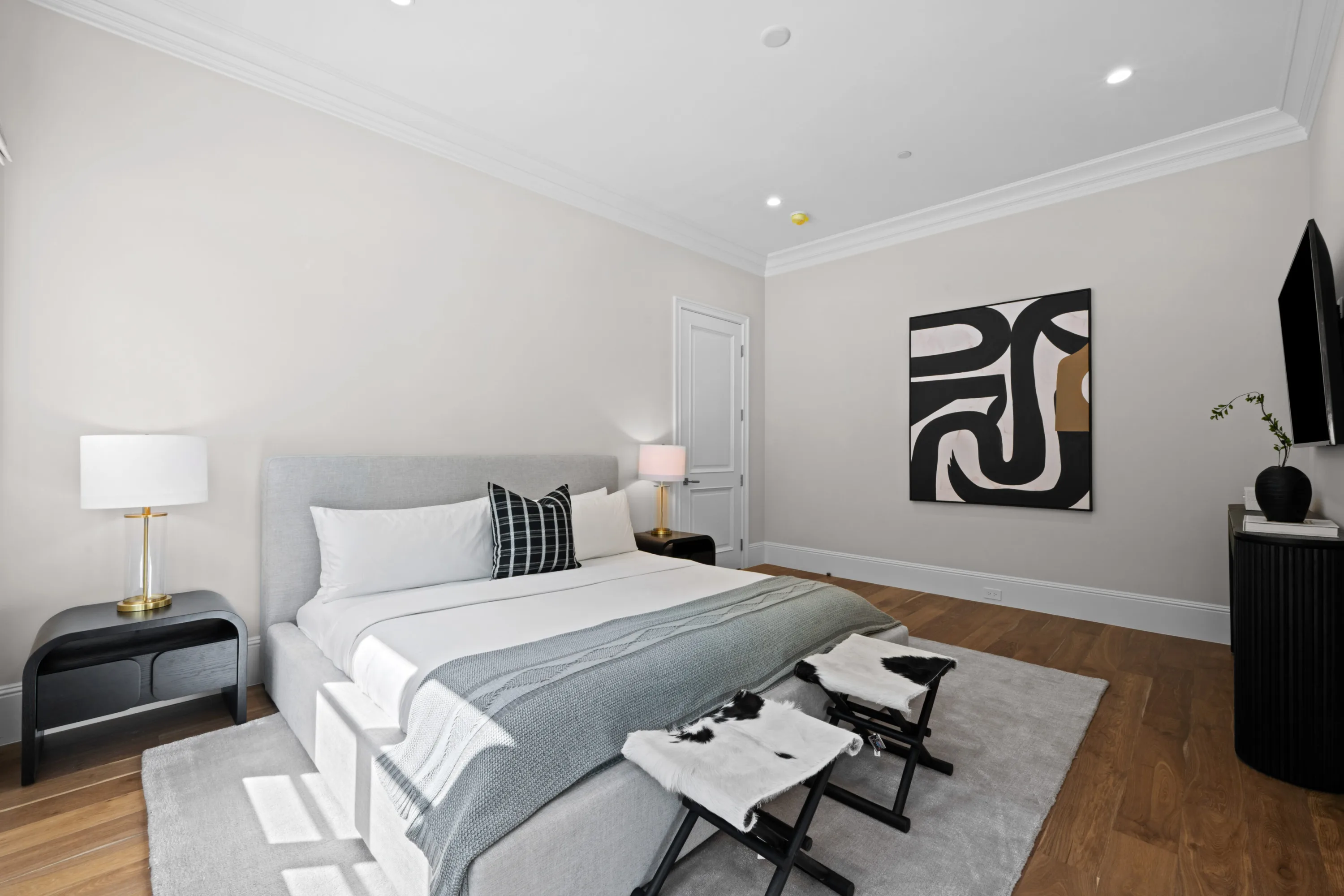 Guest suite with grey upholstered bed, brass lamps, hide stools and a graphic black-and-white artwork