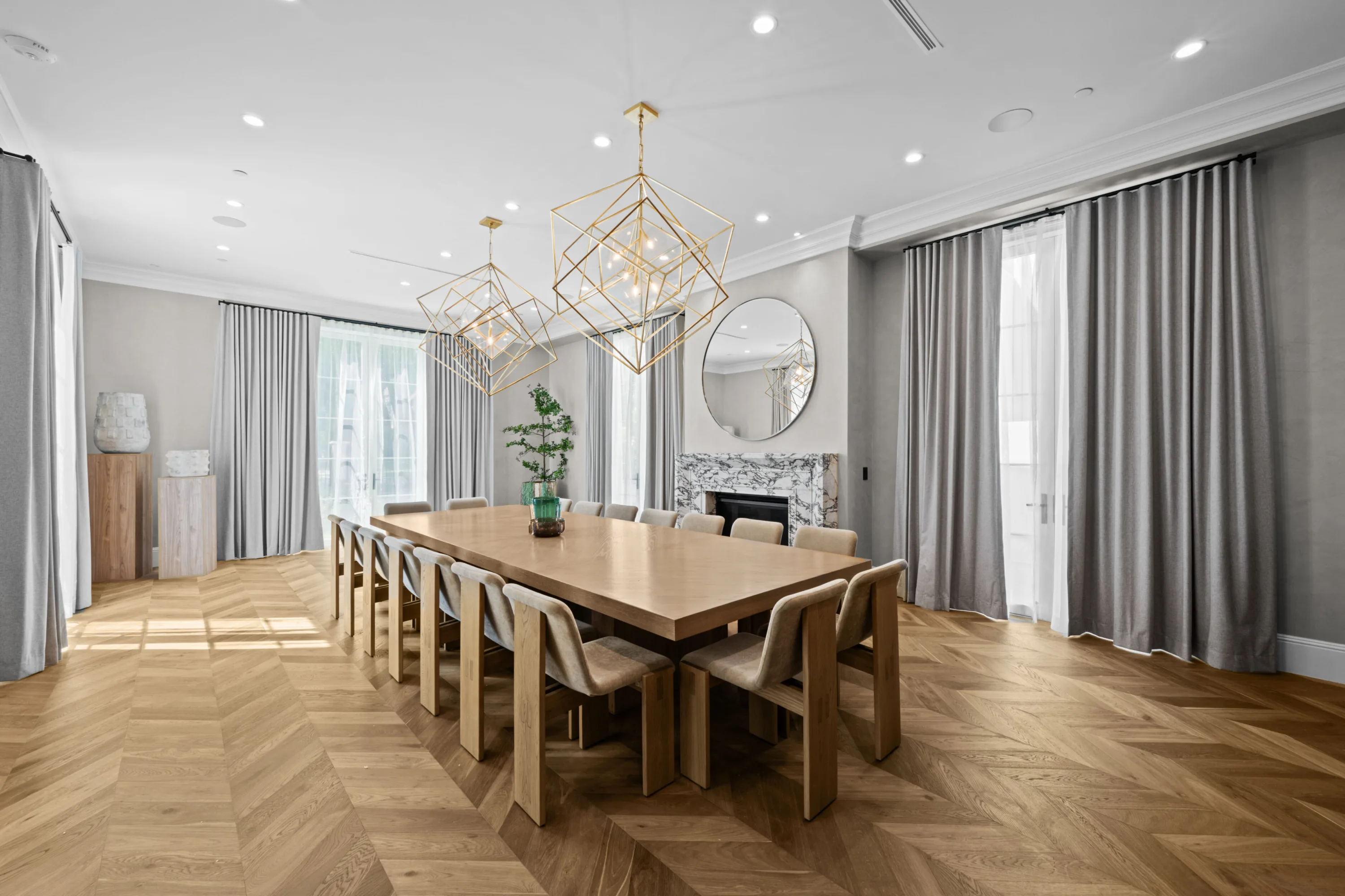 Formal dining room seating twelve beneath sculptural brass cube chandeliers, marble fireplace at the far wall