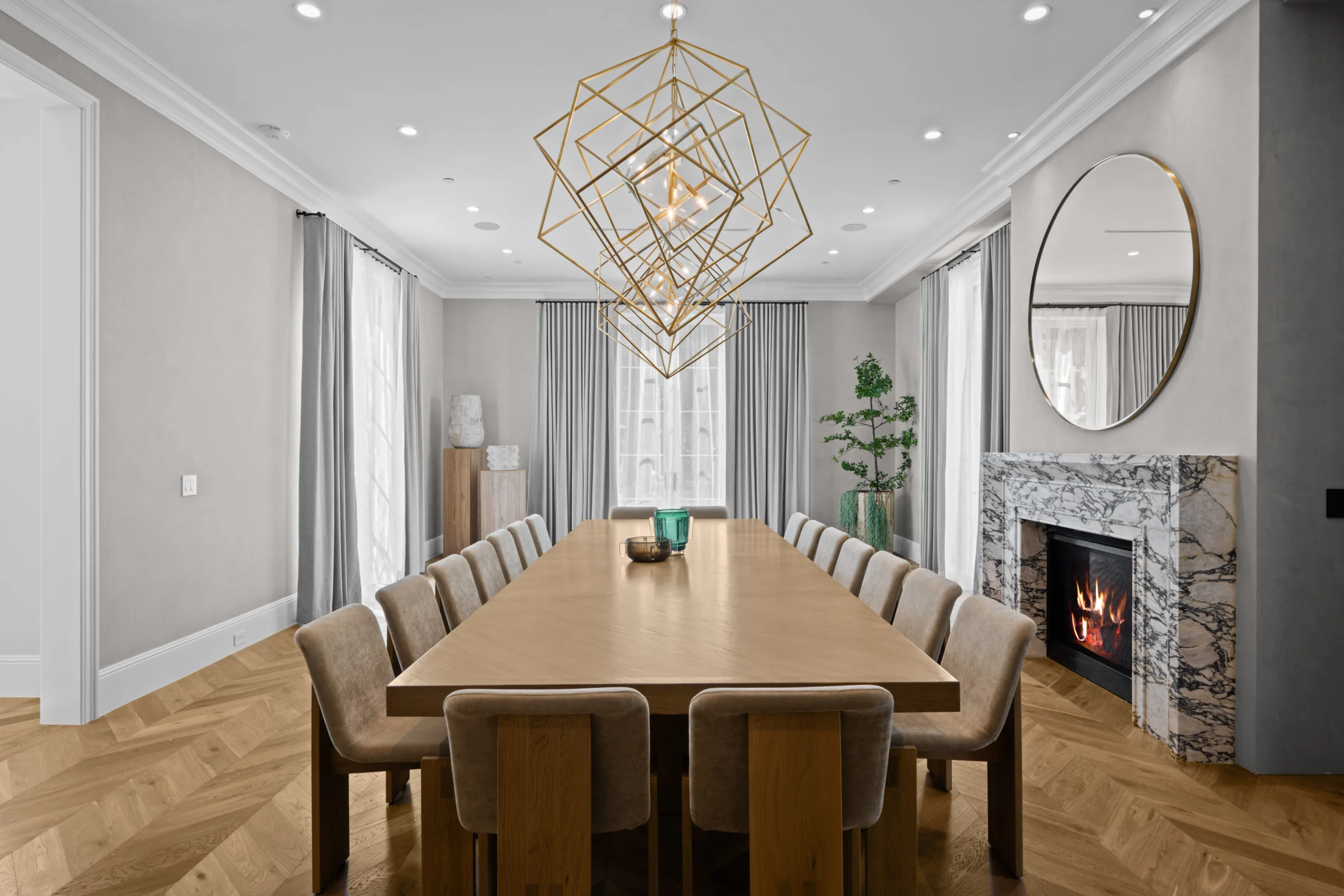 Head-on view down the dining table to the lit veined-marble fireplace and round mirror