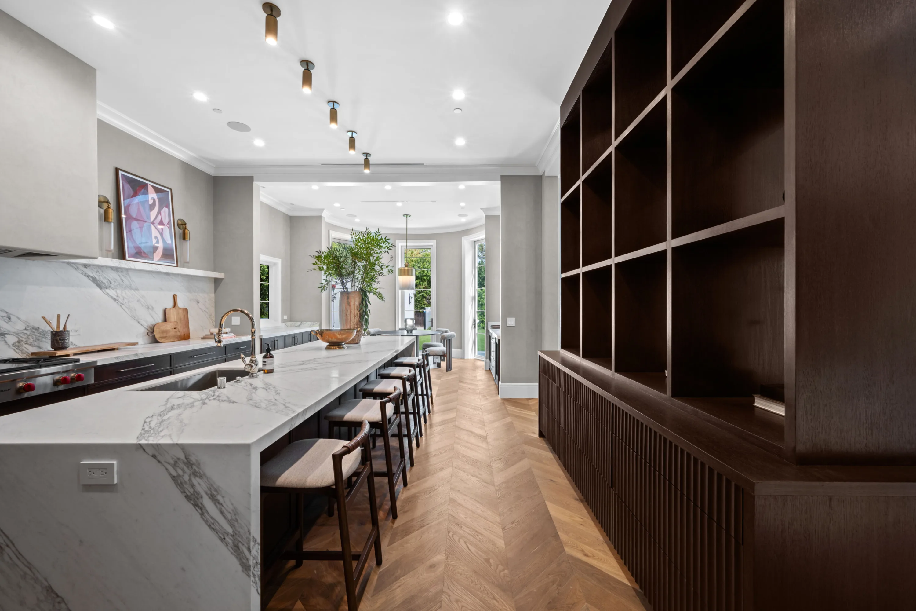 Kitchen seen along the island counter towards the garden doors, with a dark open-shelved cabinet wall opposite