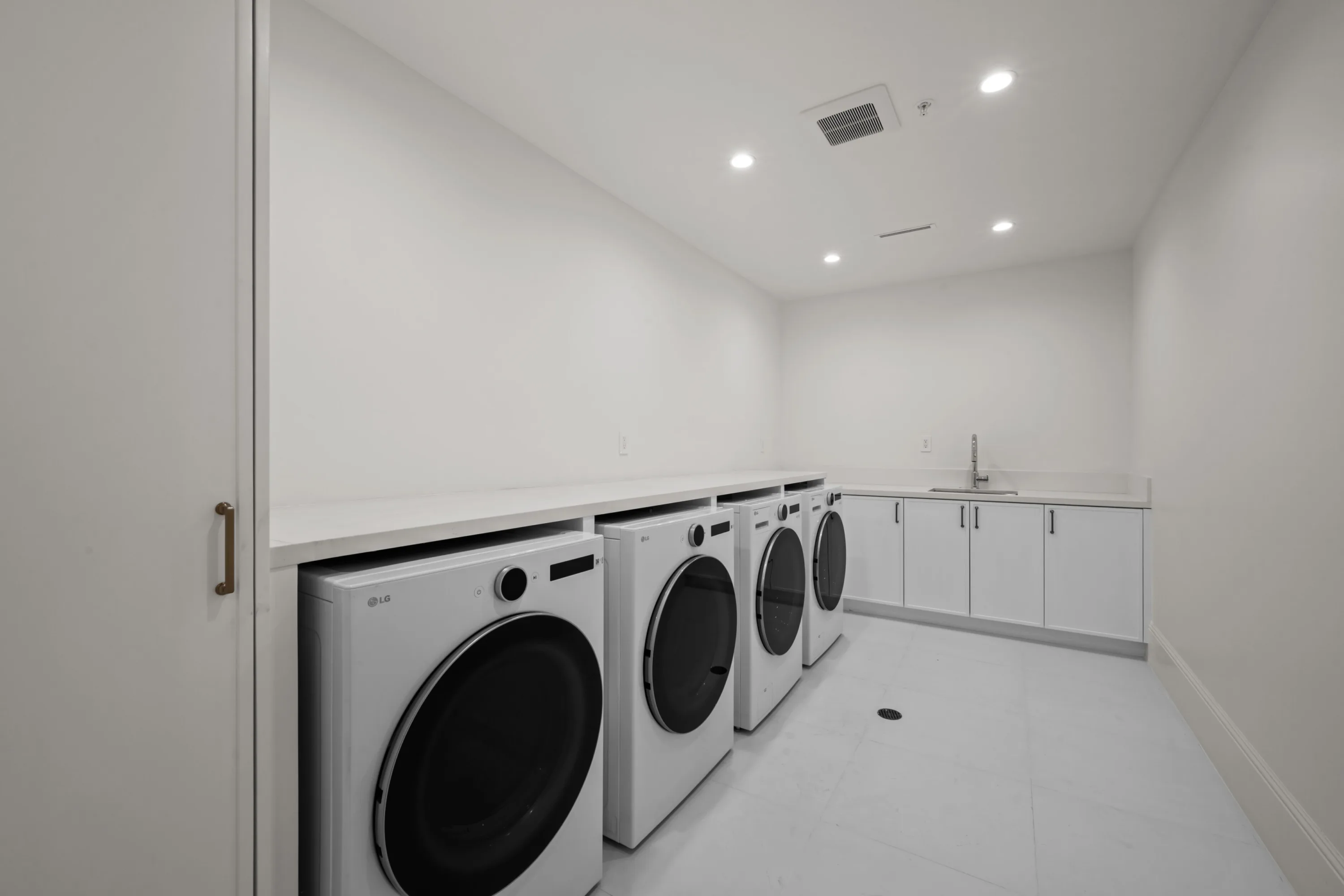 Laundry room fitted with four front-load washers and dryers, long counter and sink