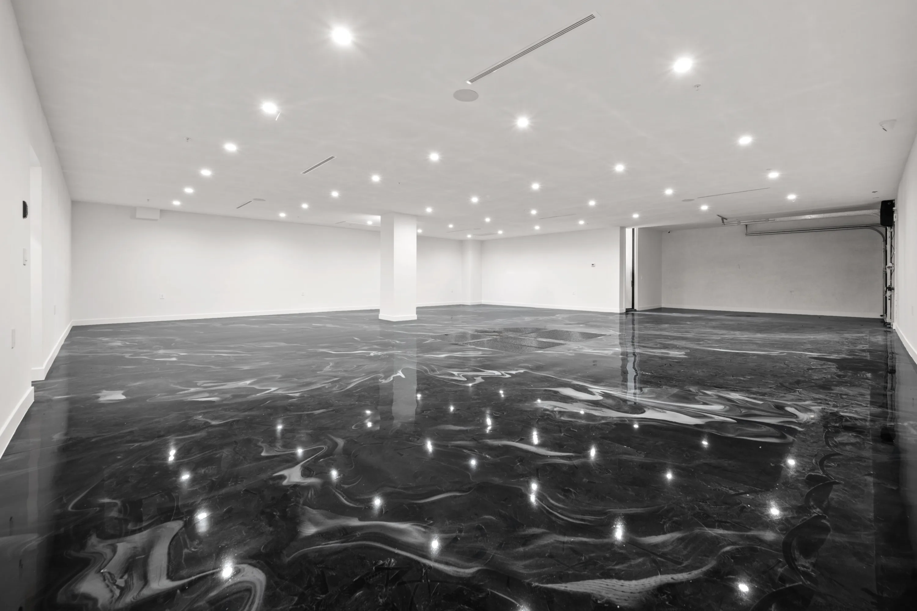 Empty lower-level garage with mirror-gloss poured epoxy floor reflecting dozens of recessed ceiling lights