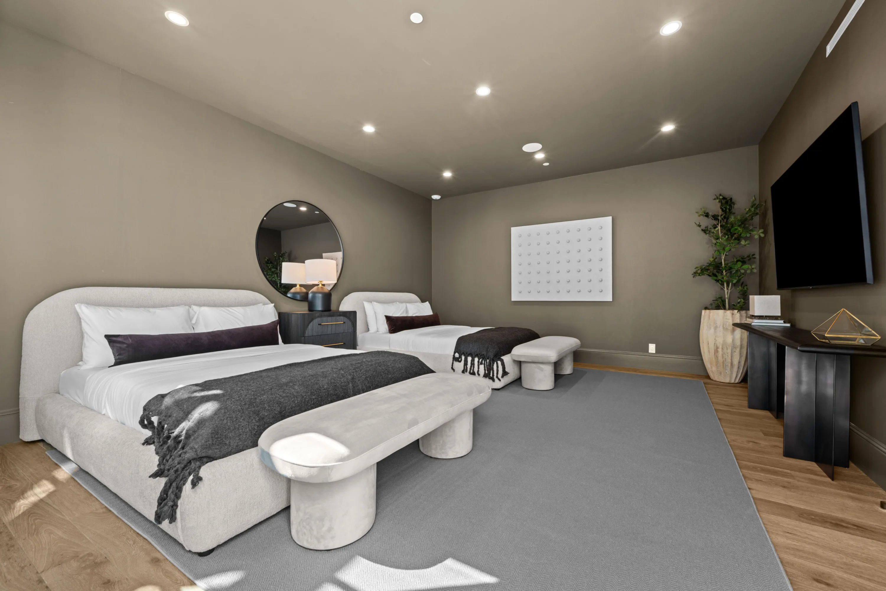 Twin-bed guest room in taupe with upholstered headboards, curved benches and a wall-mounted flatscreen