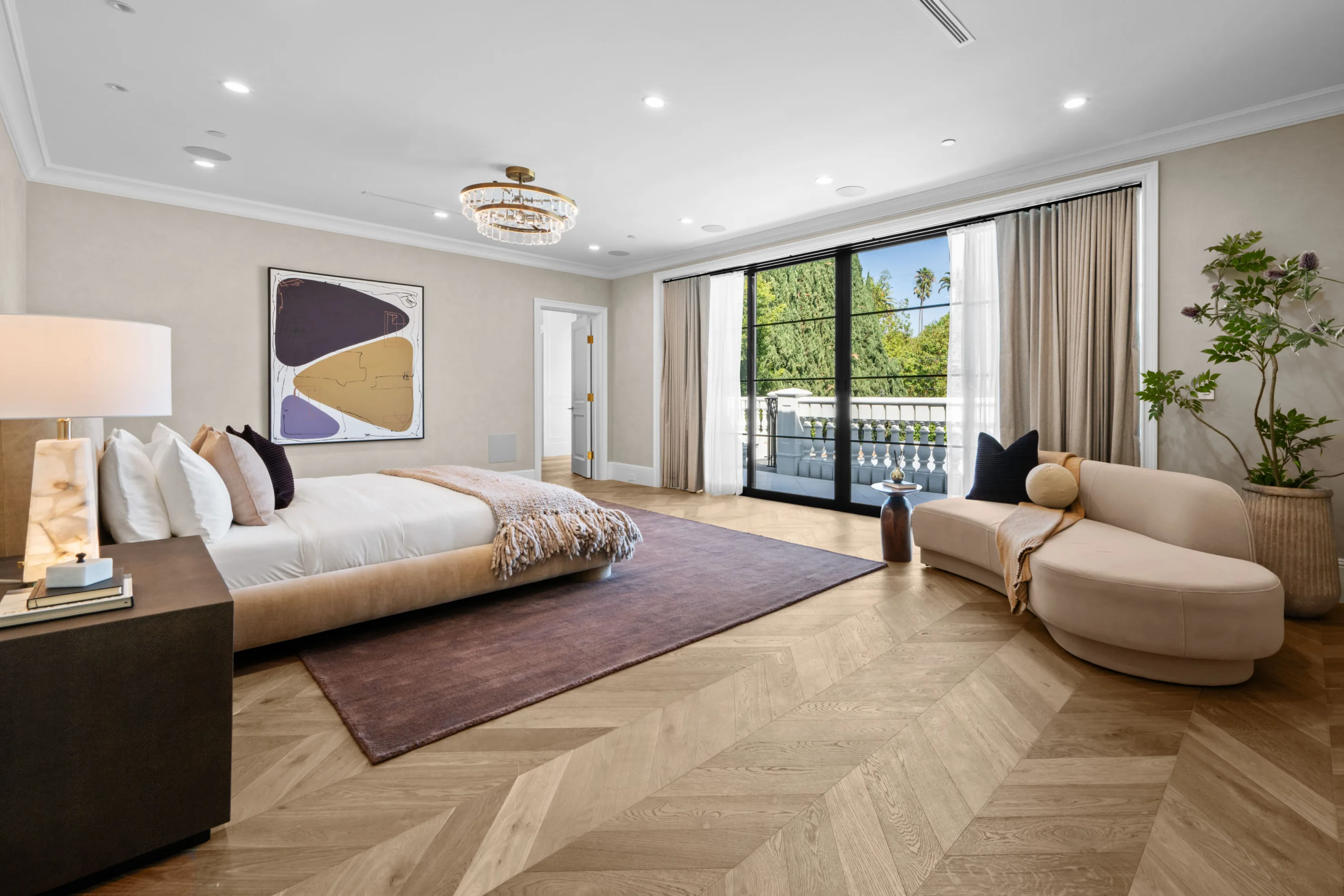 Primary suite with chevron oak floors, crystal chandelier and sliding doors to a balustraded balcony
