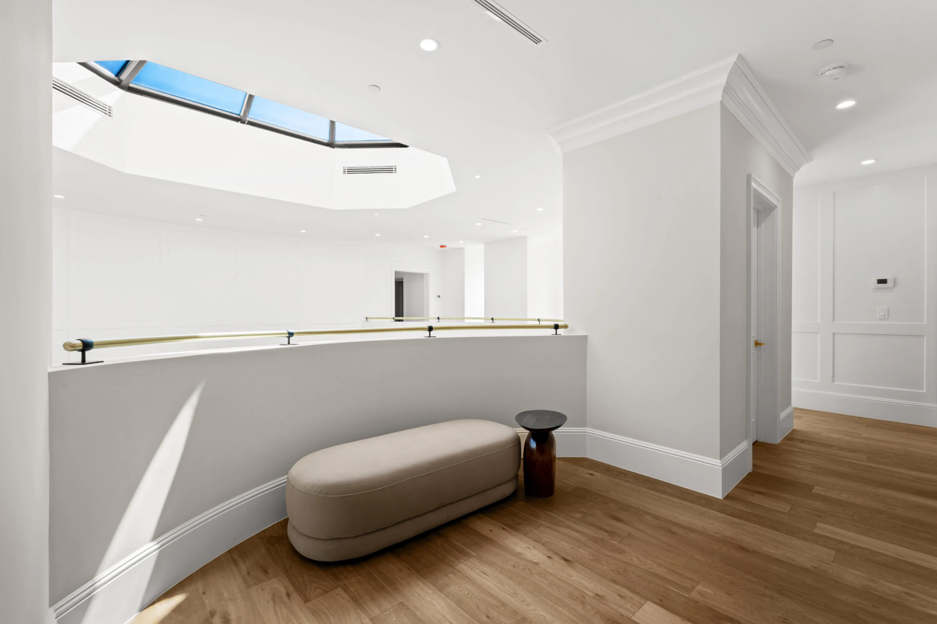 Upstairs landing under a pitched skylight, with curved gallery rail and a long upholstered bench
