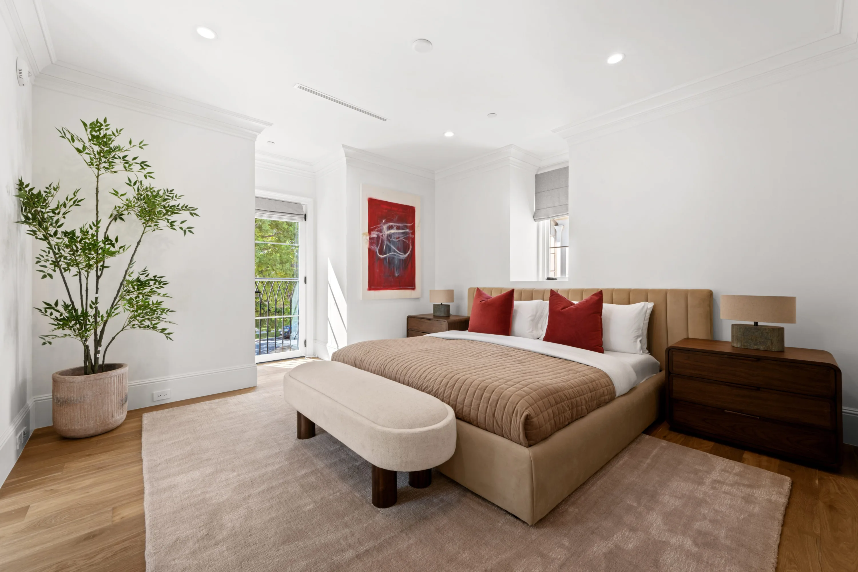 Bright guest bedroom with camel velvet headboard, red accent cushions and a Juliet balcony over the street