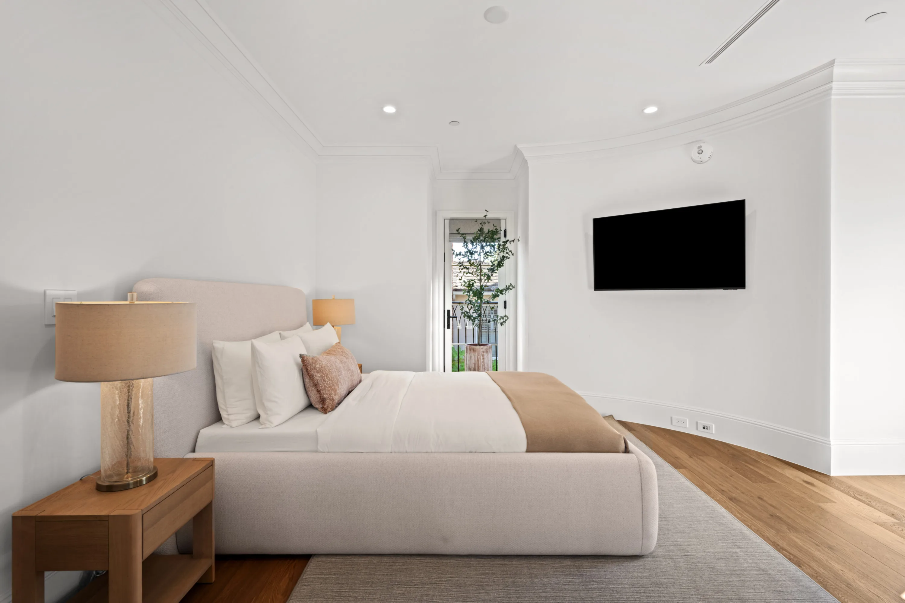 Calm white bedroom with linen-toned bed, flatscreen opposite and a door to a small garden terrace