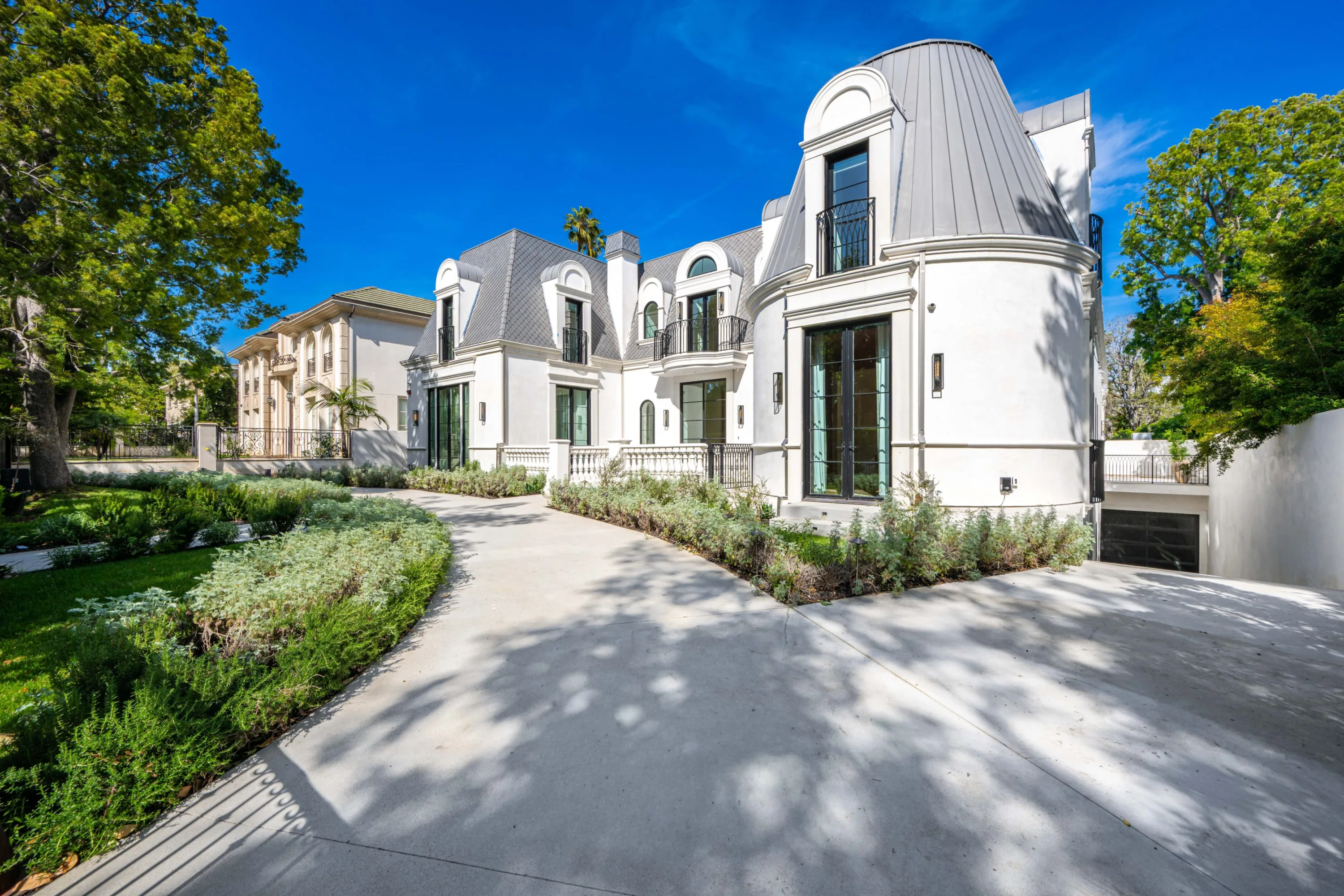 French-inspired white facade with slate mansard roof and turret, seen from the tree-shaded motor court