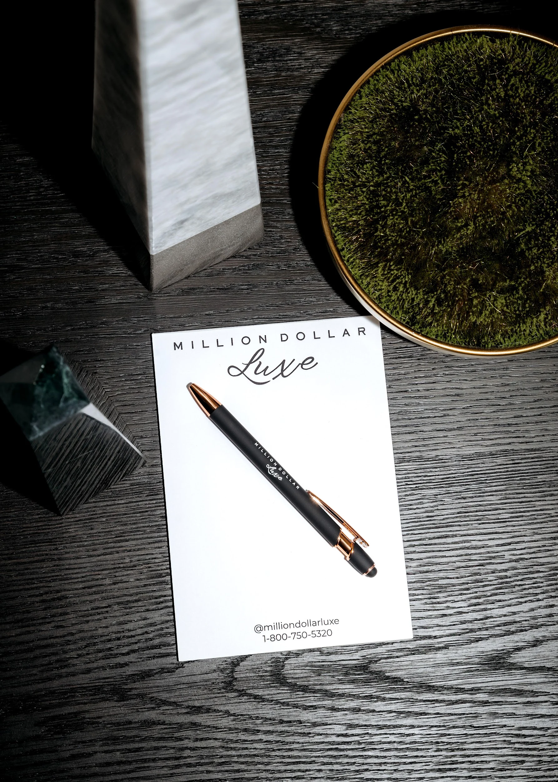 Million Dollar Luxe notepad and branded pen on a dark oak table, with @milliondollarluxe and 1-800-750-5320